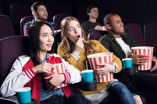 Emotional friends with popcorn and soda watching movie in cinema — Stock Photo