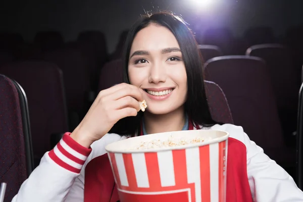 Joven asiático chica comer palomitas de maíz y viendo película en cine - foto de stock