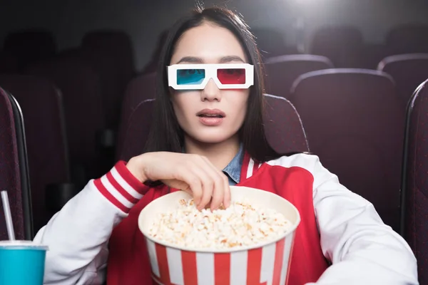 Young asian girl in 3d glasses with big basket of popcorn watching movie in cinema — Stock Photo