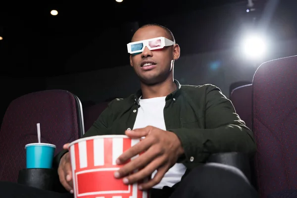 Афроамериканський чоловік в 3d окулярах їсть попкорн і дивиться фільм у кіно — стокове фото