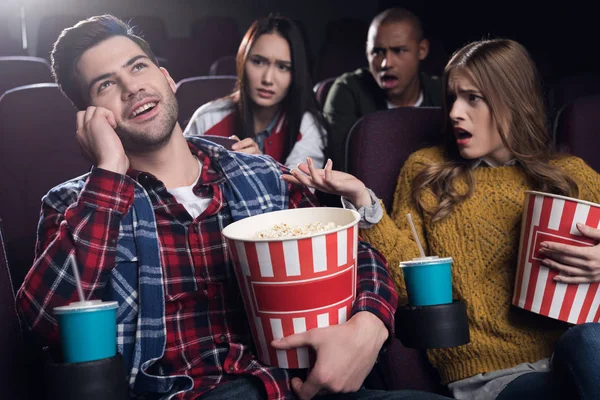 Insatisfaits des gens qui regardent l'homme parler sur smartphone au cinéma — Photo de stock