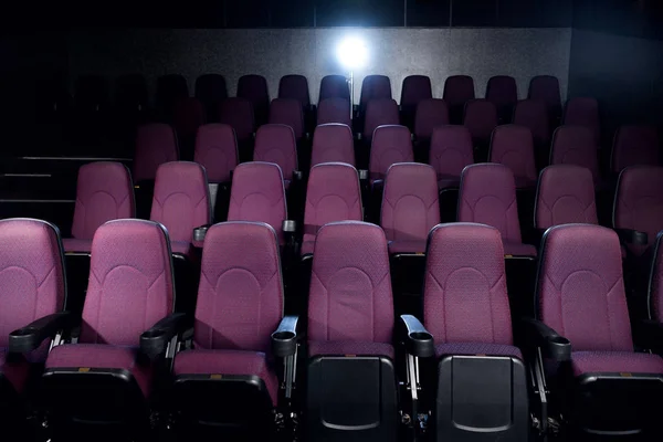 Asientos rojos en el cine oscuro vacío con luz de fondo - foto de stock