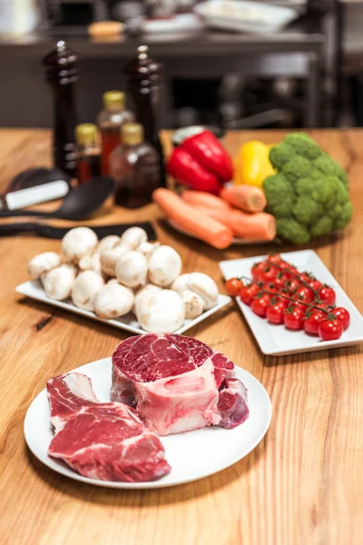 Raw meat and uncooked vegetables on wooden table — Stock Photo