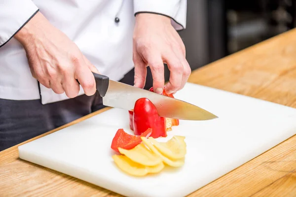 Cropped image of chef cutting red and yellow bell peppers — Stock Photo