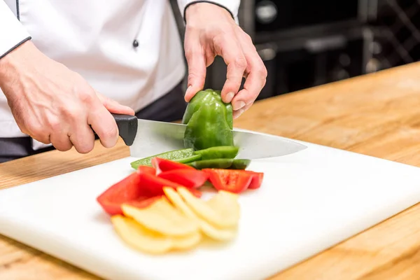 Imagen recortada de chef de corte de pimientos de colores - foto de stock