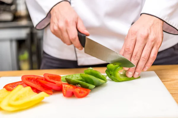 Cropped image of chef cutting colored bell peppers — Stock Photo