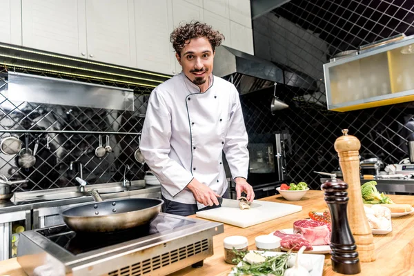 Koch schneidet Pilze in Restaurantküche und blickt in die Kamera — Stockfoto