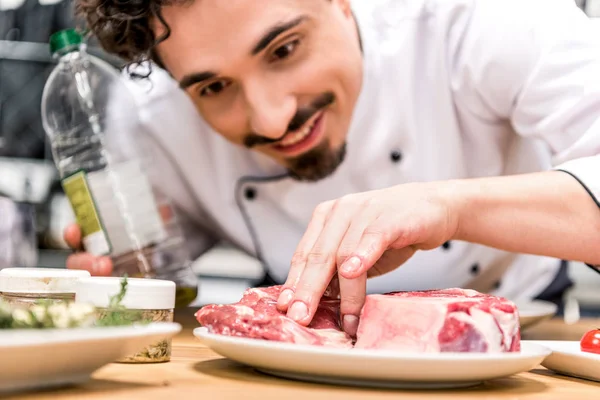 Chef sonriente añadiendo aceite a la carne cruda - foto de stock