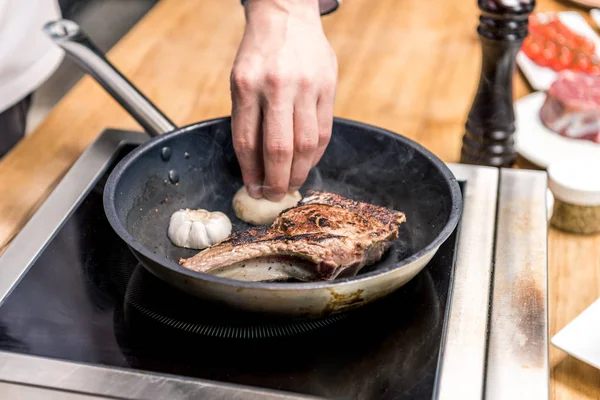 Imagem cortada de chef colocando alho para fritar carne — Fotografia de Stock