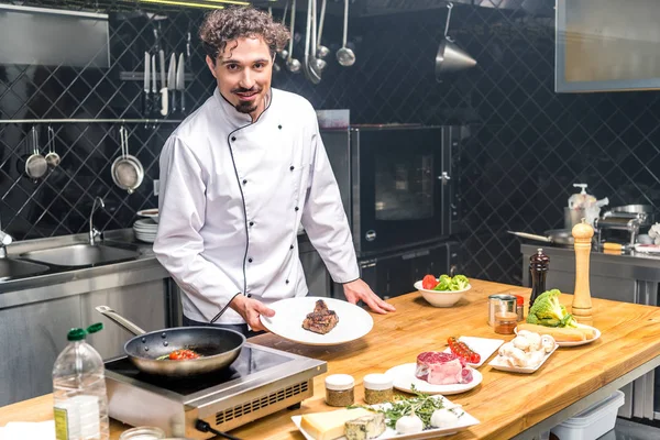 Улыбающийся шеф-повар держит тарелку с жареным мясом — стоковое фото