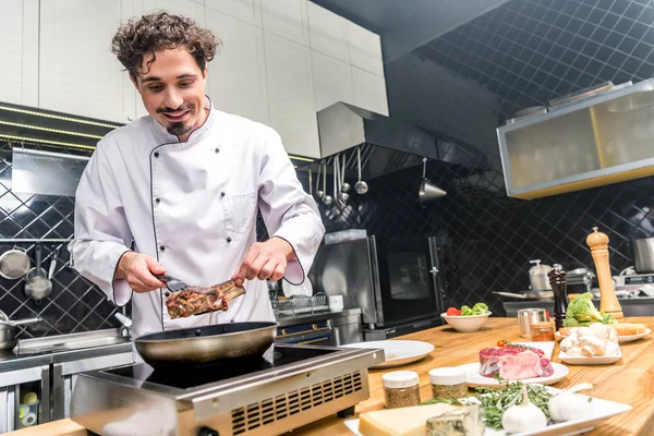 Chef sorrindo fritar carne na cozinha do restaurante — Fotografia de Stock