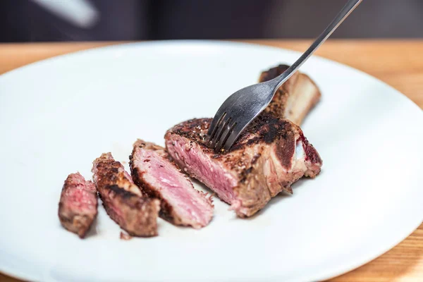Смажене м'ясо з виделкою на білій тарілці на дерев'яному столі — Stock Photo