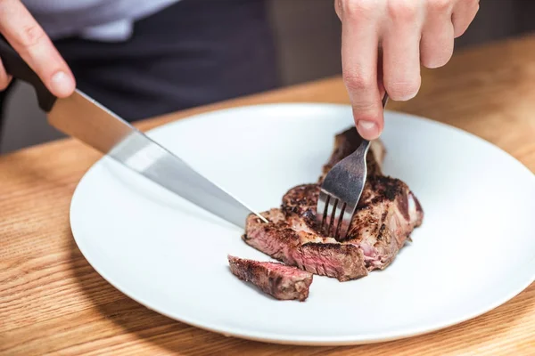 Cropped image of chef cutting fried meat with knife and fork — Stock Photo