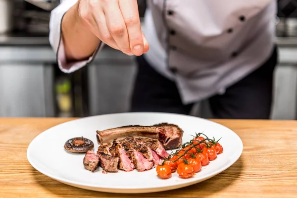 Abgeschnittenes Bild vom Koch, der gekochtes Fleisch mit Gemüse mit Pfeffer würzt — Stockfoto