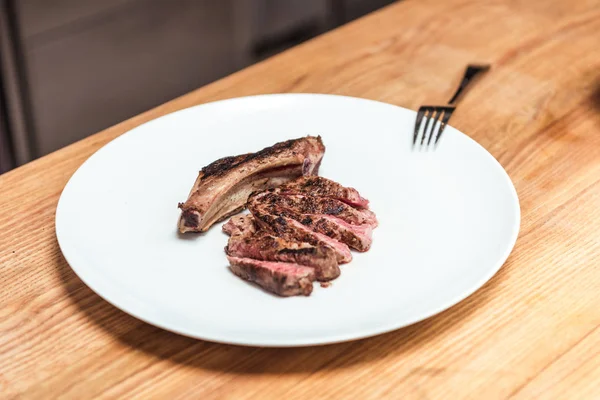 Gebratenes Fleisch auf weißem Teller auf Holztisch — Stockfoto