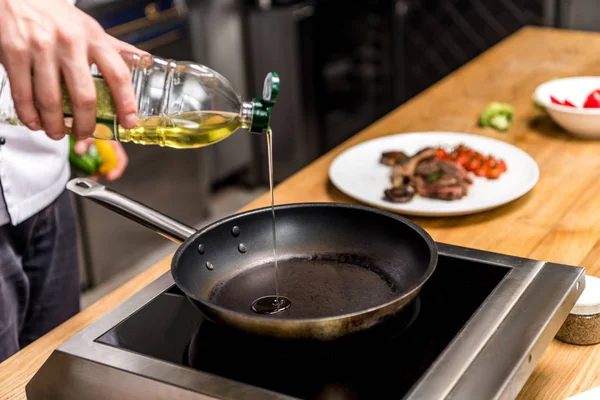 Cropped image of chef pouring oil on frying pan — Stock Photo