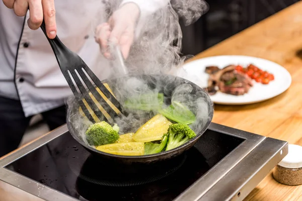 Image recadrée du chef en remuant les poivrons avec du brocoli sur la poêle — Photo de stock