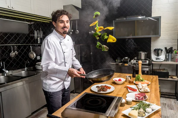 Smiling chef tossing up frying bell peppers with frying pan — Stock Photo