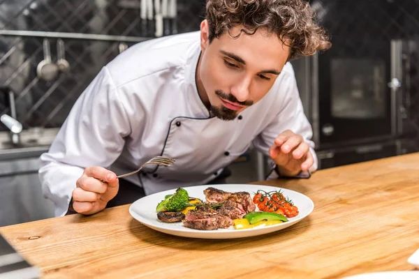 Guapo chef de pie con tenedor encima de las verduras fritas con carne — Stock Photo