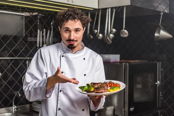 Chef bonito mostrando legumes cozidos com carne no prato — Fotografia de Stock