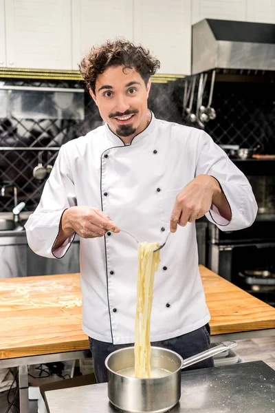 Chef sorridente in piedi con pasta sulla forchetta e guardando la macchina fotografica — Foto stock