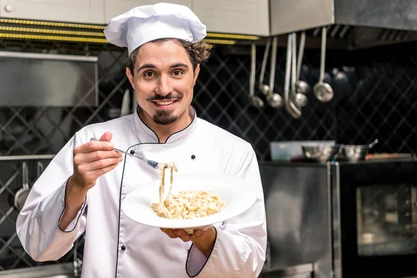 Chef souriant tenant assiette avec pâtes et fourchette dans les mains — Photo de stock