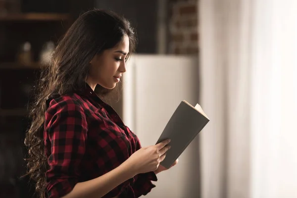 Vue latérale de fille sexy en chemise à carreaux livre de lecture à la maison — Photo de stock