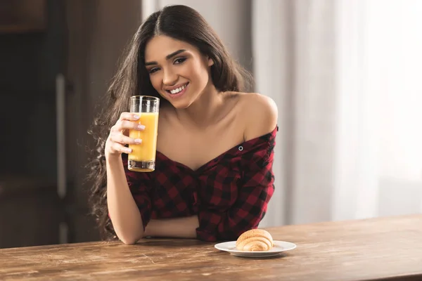 Sexy Mädchen im karierten Hemd isst Croissant und trinkt Orangensaft zum Frühstück — Stockfoto