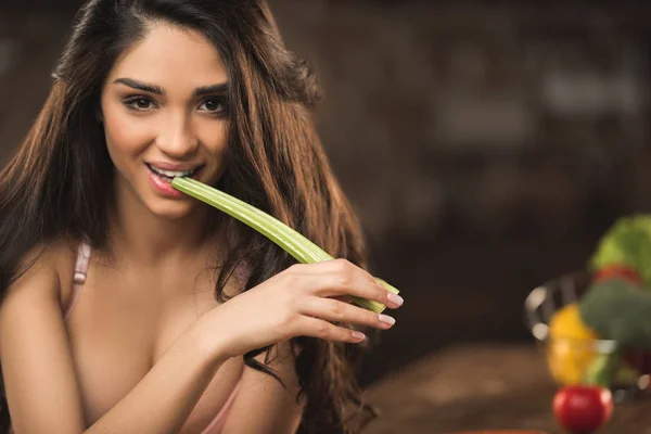 Sexy jeune femme en sous-vêtements manger céleri et sourire à la caméra — Photo de stock