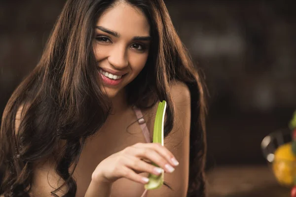 Séduisante jeune femme mangeant du céleri et souriant à la caméra — Stock Photo