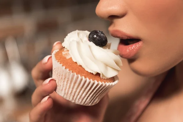 Primer plano parcial vista de sensual joven comiendo delicioso cupcake - foto de stock