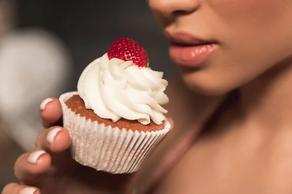 Tiro cortado de sensual jovem segurando delicioso cupcake perto de lábios — Fotografia de Stock