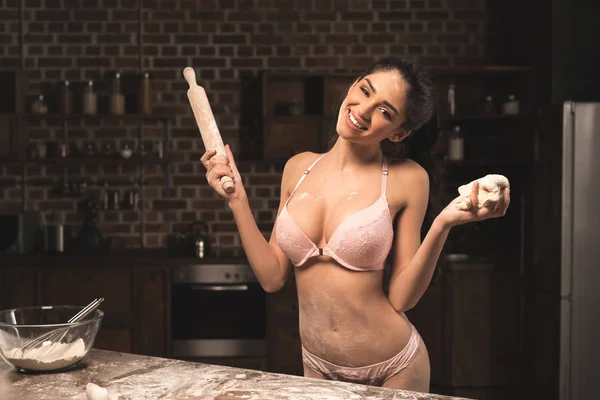 Sexy junge Frau in Unterwäsche hält Nudelholz mit Teig und lächelt in die Kamera — Stockfoto