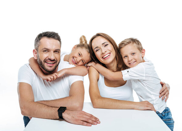 Улыбающаяся семья в белых футболках обнимается
 