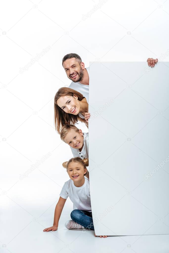Smiling family in white t-shirts holding blank white card and looking at camera isolated on white