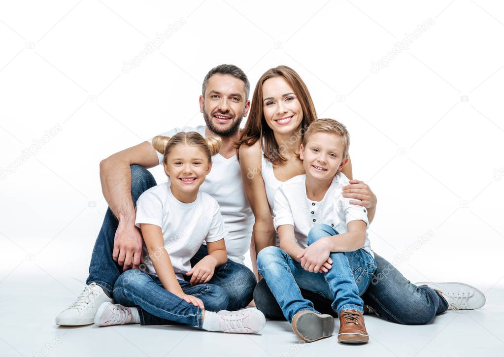 Happy family with two children sitting together and looking at camera isolated on white
