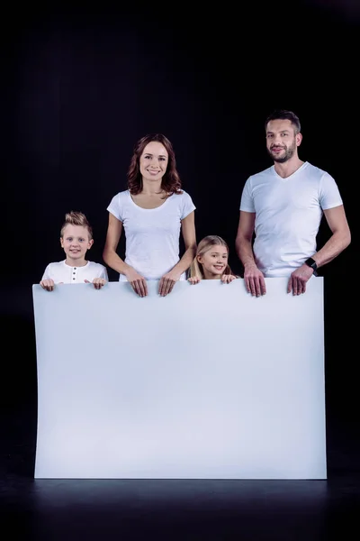 Family standing with blank white card — Stock Photo