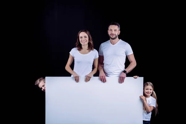 Family standing with blank white card — Stock Photo