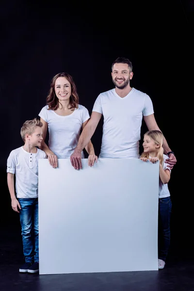 Familia sonriente sosteniendo tarjeta en blanco - foto de stock