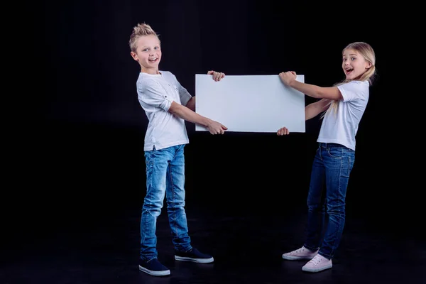 Hermanos sonrientes con tarjeta en blanco - foto de stock