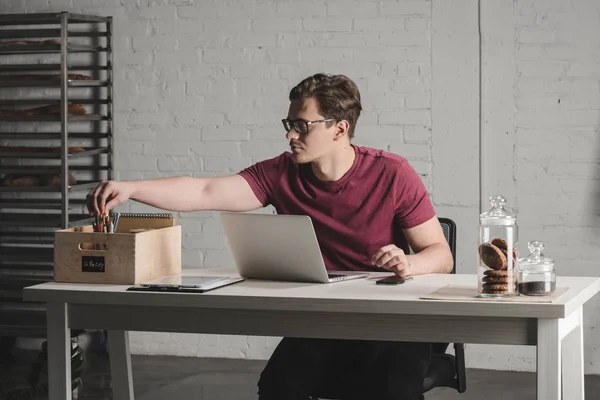 Man working with laptop at bakery — Stock Photo