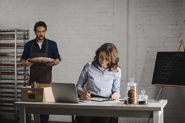 Woman making notes in bakehouse — Stock Photo