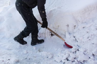 Kişi kırmızı kürek kar atar.