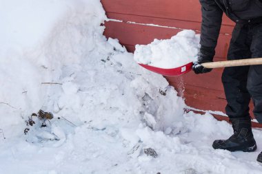 Kişi kırmızı kürek kar atar.