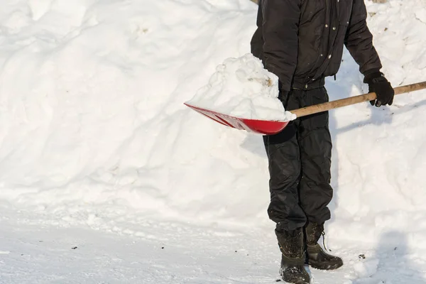 De persoon gooit een rode schop sneeuw. — Stockfoto