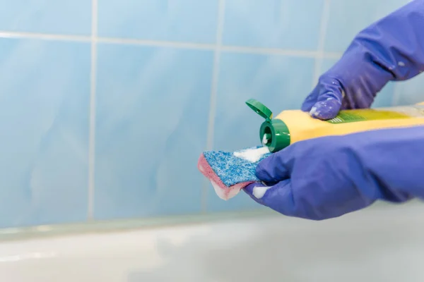 The girl cleans up in the bathroom, pour cleaning agent on the sponge, the girl cleans up in rubber gloves