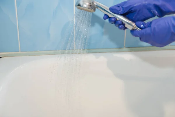 The girl cleans the bath, the water in the shower, clean the bath, the girl cleans the white bath, with rubber glove — Stock Photo, Image