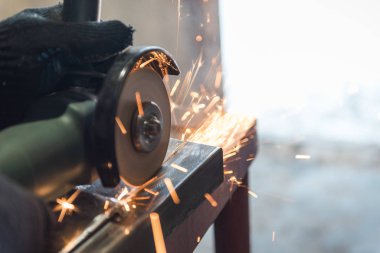 Açısal öğütme makinesiyle metali kes. Kıvılcımlar uçuşuyor. İnşaat aleti öğütücüsü. Bir adam metali kesiyor. Güvenlik için eldiven tak.. 