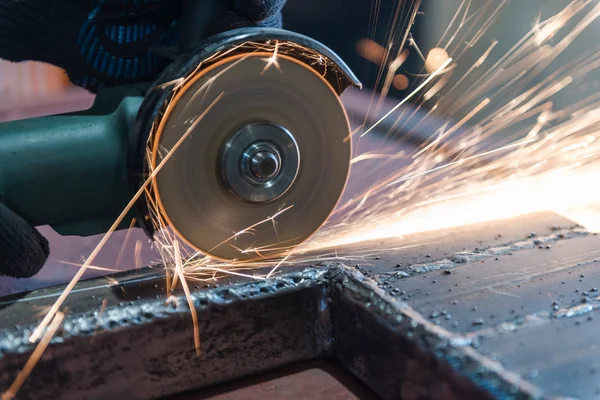Açısal öğütme makinesiyle metali kes. Kıvılcımlar uçuşuyor. İnşaat aleti öğütücüsü. Bir adam metali kesiyor. Güvenlik için eldiven tak.. 