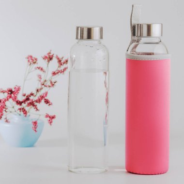 İki temiz cam şişe. Biri pembe bir kutuda, temiz suyla birlikte. Ayarlanmış Instagram